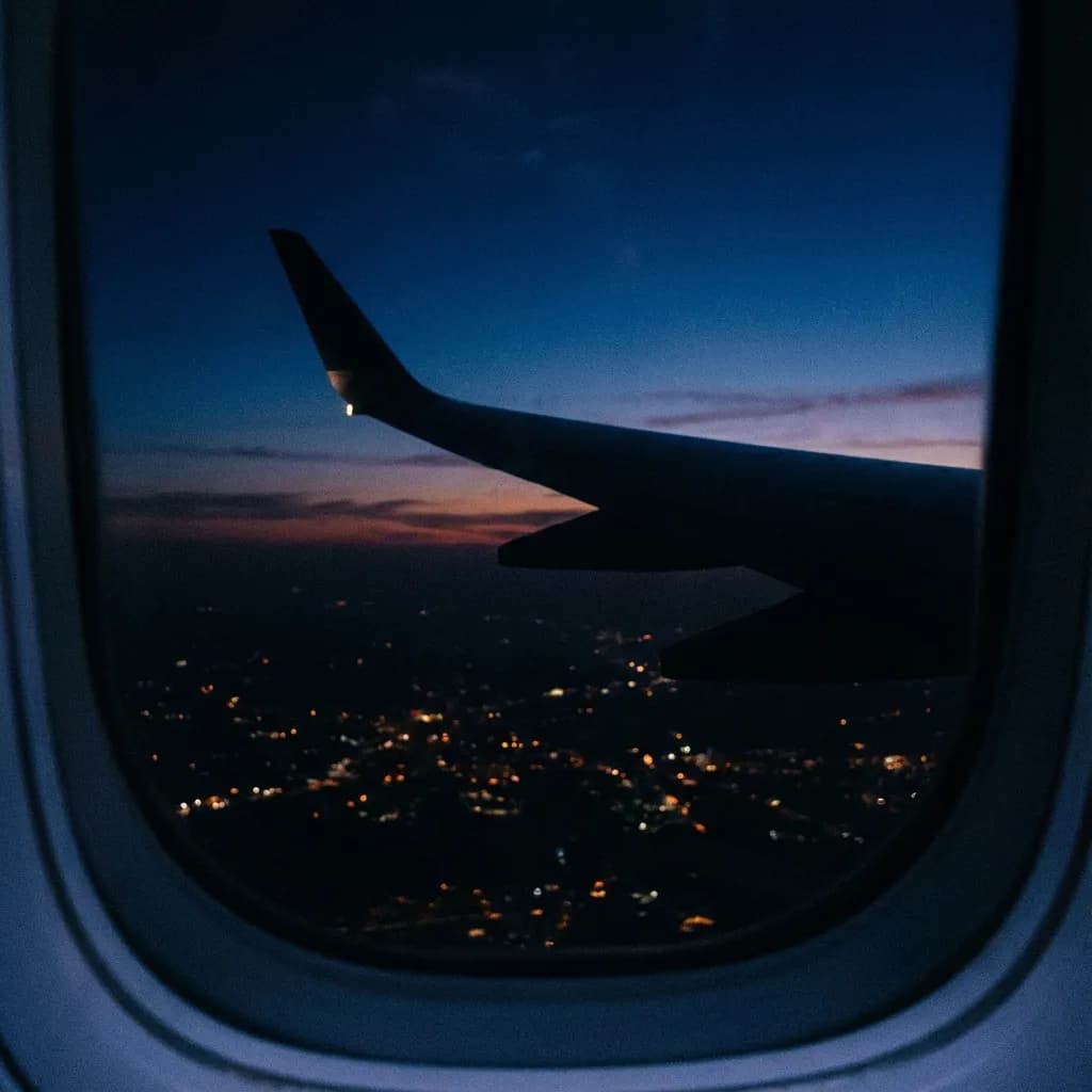 An airplane wing above the city lights at sunset